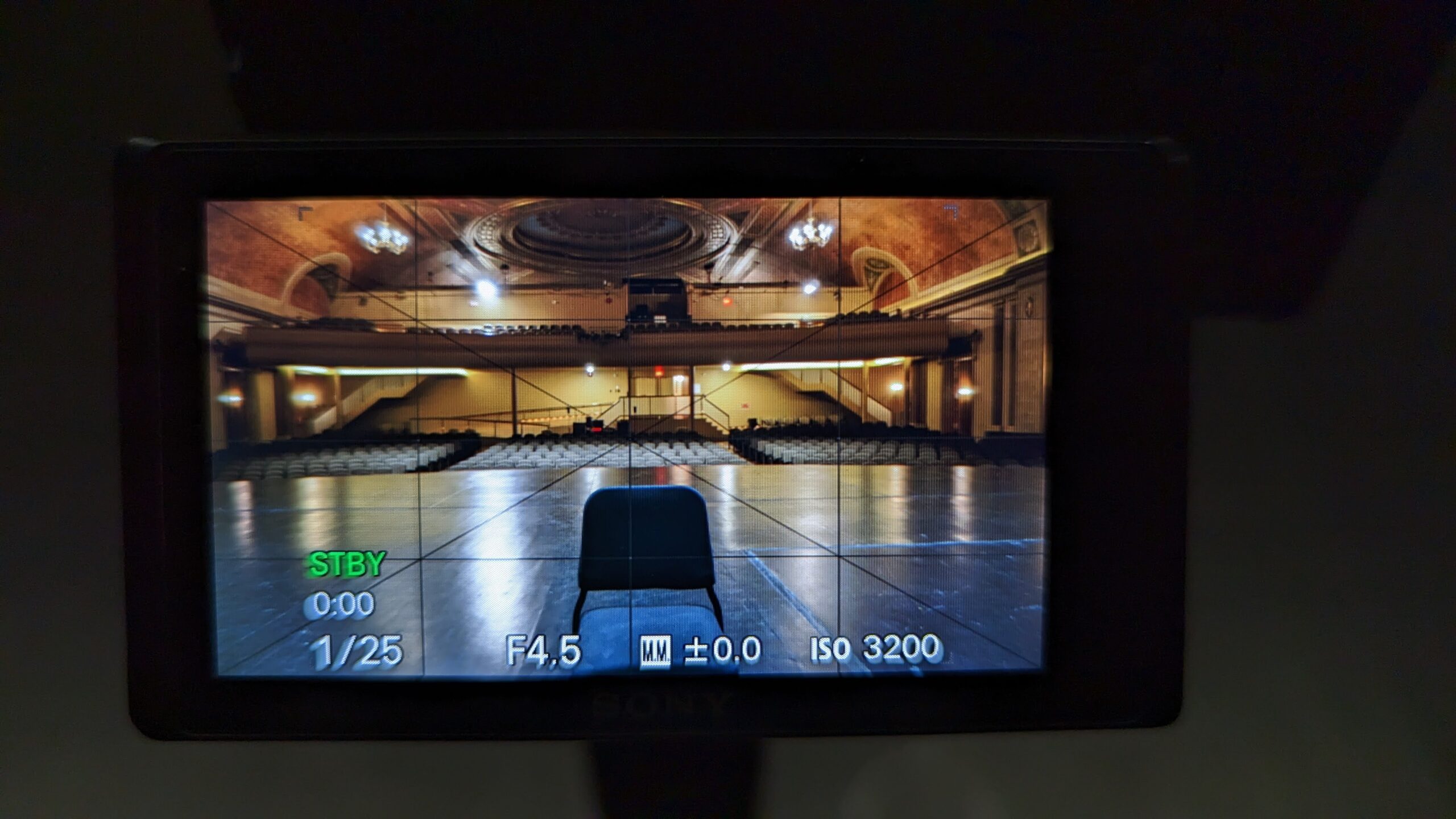 Video camera screen showing a chair on an empty stage.